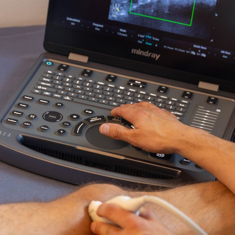 Ultraschall Dr. Güths Hand, die ein Ultraschallgerät bei einer Knieuntersuchung bedient. Auf dem Bildschirm ist das Ultraschallbild zu sehen.
